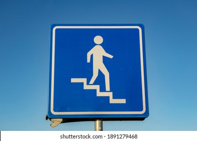 Monochrome dark blue square sign and graphic showing person descending stairs against clear blue sky