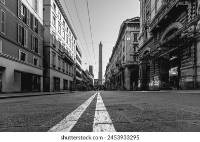 Monochrome image of a Bologna street taken from a low angle, focusing on the converging road lines that lead toward the towering Asinelli Towers in the background - Powered by Shutterstock