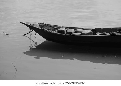 Monochrome image capturing an old wooden boat with containers resting on still water. - Powered by Shutterstock