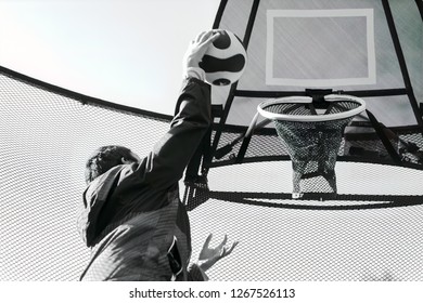 Monochrome Image Of A Kid Shooting A Basketball Through A Trampoline Mounted Basketball Hoop