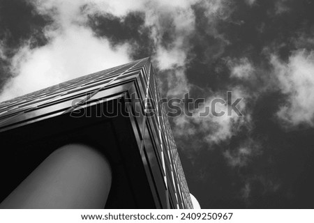 Monochrome image of a modern skyscraper reaching into a sky filled with textured clouds, showcasing bold architecture and upward perspective
