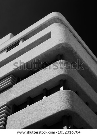 monochrome image of an old brutalist concrete tower block with rounded textured corners against a dark sky