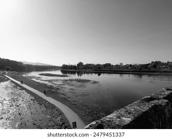 A monochrome image of a scenic view of a tranquil, artificial lake with a nearby walkway with people - Powered by Shutterstock