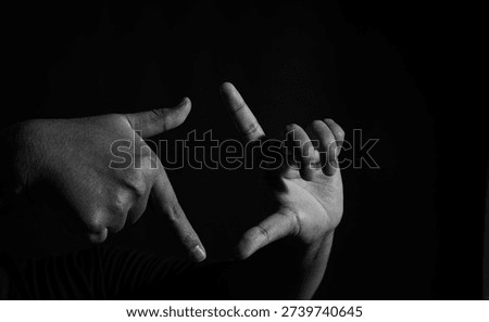 Monochrome image of two hands creating a framing gesture, isolated on black backdrop with strong contrast and artistic shadow detail.