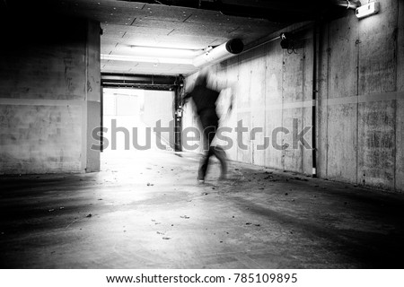 Monochrome of a man fleeing a grungy underground parking. 