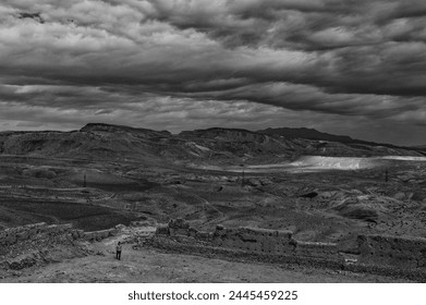 Monochrome Morocco: Summit of Aït Benhaddou, a solitary figure contrasts the vast desert expanse under a brooding overcast sky. - Powered by Shutterstock