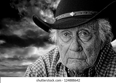 Monochrome Of An Old Man Wearing A Black Felt Hat Against A Stormy Cloudy Sky