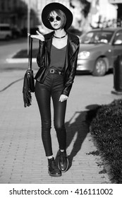 Monochrome Outdoor Full Body Portrait Of Young Beautiful Fashionable Lady Walking On The Old Street. Model Wearing Stylish Leather Clothes. Girl Looking At Camera. Female Fashion. City Lifestyle