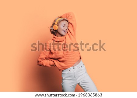 Monochrome photo of a caucasian woman listening to music on headphones posing on a orange studio wall