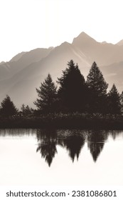 A monochrome photo of the Lago Di Joux, a small lake in the Italian Alps,silhouettes of fir trees reflectin in the water, mountains in the background, white sky, sepia, bleached effect, copy space
