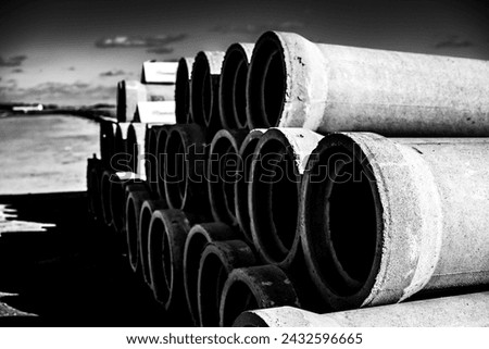 Monochrome photo of stacked concrete pipes against sky