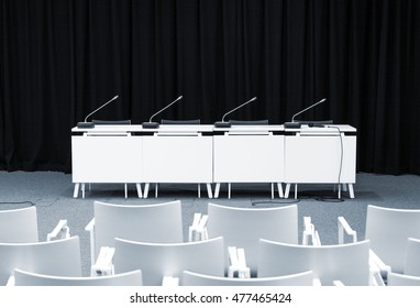 Monochrome Picture Of Empty Press Conference Room With Seats, Stand Table And Microphones