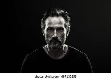 Monochrome Portrait Of Mid Aged Lonely Man. Black And White Photo Of Male In Black T-shirt On Dark Backdrop.