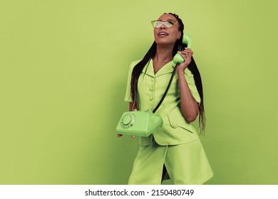 Monochrome portrait of smiling african girl wearing retro style outfit holding vintage phone isolated on green background. Concept of beauty, art, fashion, youth, sales and ads. Copy space for ad.