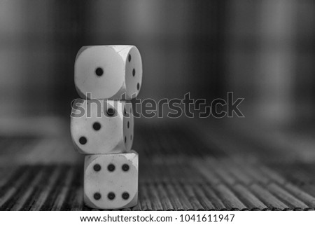 Monochrome Stack of three white plastic dices on brown wooden board background. Six sides cube with black dots. Number 1, 3, 6
