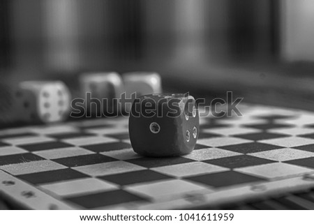 Monochrome Stack of three white plastic dices and one red dice on brown wooden board background. Six sides cube with black dots. Number 1.