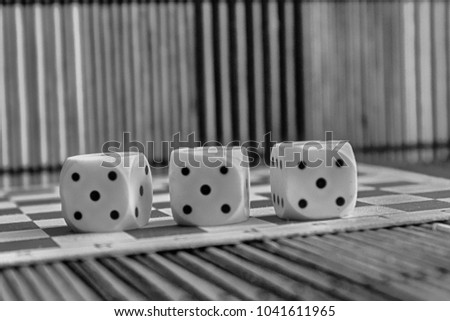 Monochrome Stack of three white plastic dices on brown wooden board background. Six sides cube with black dots. Number 5.