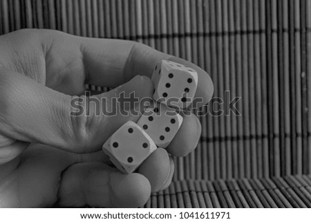 Monochrome Stack of three white plastic dices in man's hand on brown wooden table background. Six sides cube with black dots. Number 4, 6, 6