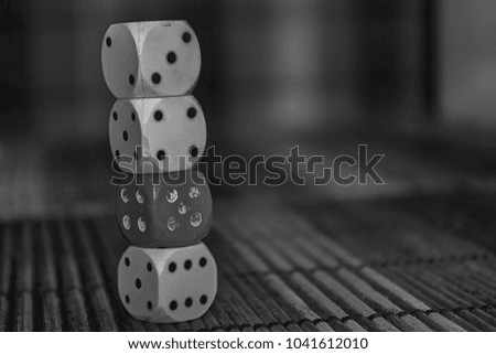 Monochrome Stack of three white plastic dices and one red dice on brown wooden board background. Six sides cube with black dots. Number 3, 4, 5, 6