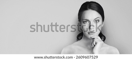 Monocrome image of puzzled thinking thoughtful cute brunette dark hair woman hold hand chin and looking seious strictly, isolate plain background with text free space. Black and white portrait.