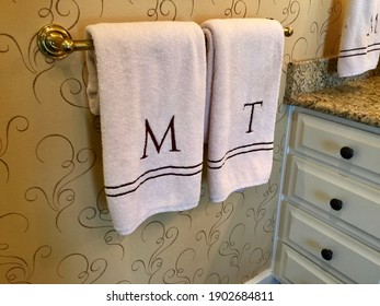 Monogrammed M and T towels hanging on a towel rod in a bathroom.