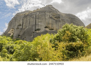 Monolithic rock with a historic monastery cliffside, amidst lush greenery in Meteora, Greece - Powered by Shutterstock