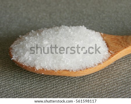 Monosodium Glutamate (MSG or E621) on wooden spoon with grey fabric background.