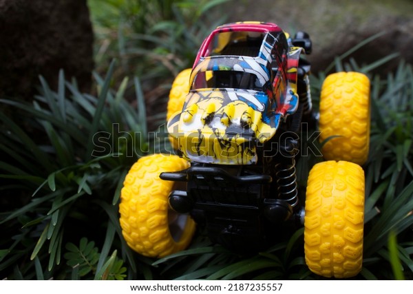 Monster car toys\
standing on stone and grass. Vehicles toy. Simple cheap toys for\
children, kids playing car, abstract concept nobody. Bogor, 07\
Agustus 2022, Indonesia