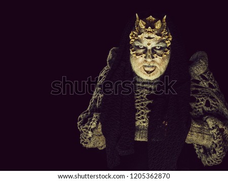 Monster in grey knitted sweater. Demon with scarf on head isolated on black. Horror and fantasy concept. Alien or reptilian makeup with sharp thorns and warts. Man with dragon skin, copy space