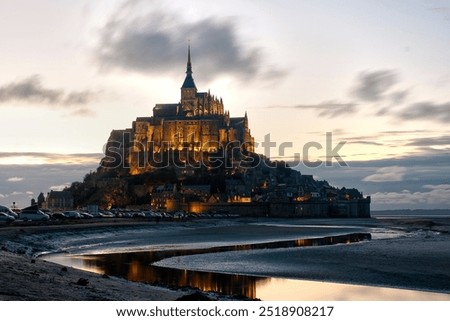 Mont Saint Michel at dusk. Low tide and wind moving the clouds; movement captured by shutter speed. Normandy.