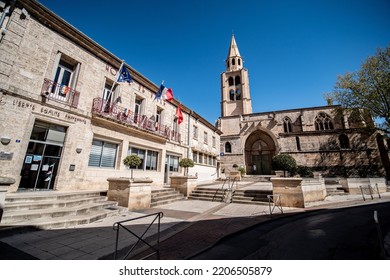 Montagnac, France - September The 20th 2021 : Town Hall With The French Flags On The Left And The Church On The Right With Its Bell. Stairs In Front, A Sunny Town In The South Of France, Blue Sky