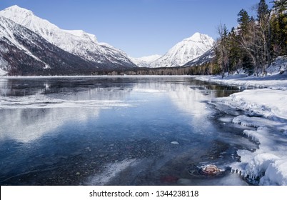 Montana Lake In Winter:  Snow Covered Mountains Reflect From The Icy Surface Of Lake McDonald In Glacier National Park.
