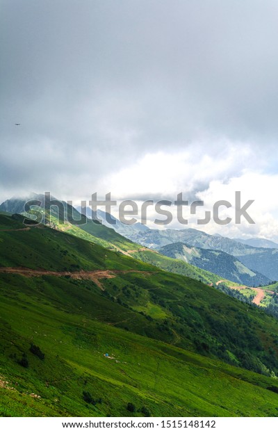 Montane grasslands in the mountains of\
Sochi near Rosa Khutor resort with road and the mountains of Aibga\
Ridge in the background in summer. Sochi,\
Russia.