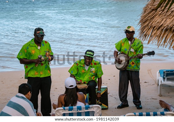 MONTEGO BAY,\
JAMAICA - JANUARY 09, 2017: Three Jamaican Musicians on the beach\
playing mento - Jamaican folk music, they play on banjo, hand drums\
and Jamaican Congo Drums, front\
view