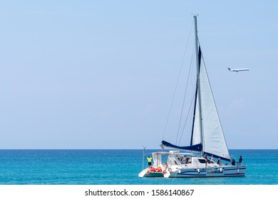 Montego Bay, Jamaica - March 19 2018: Caucasian And African American Tourists Enjoying A Catamaran Cruise On Sunny Day On The Ocean In Montego Bay City. Aircraft Landing At MBJ Airport In Background.