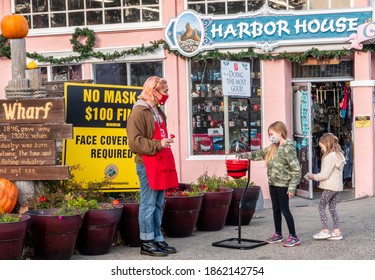 Monterey, California - November 21, 2020: Two Girls Put Money Into The Red Kettle Of The Salvation Army, In Front Of The Harbor House At The Old Fisherman's Wharf During Covid19 Mask Mandate.