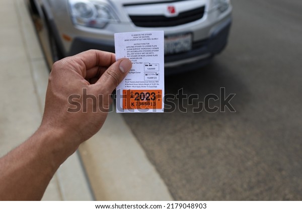 Monterey,
California, USA - July 15, 2022: African-American man holding 2023
car registration in front of silver
car