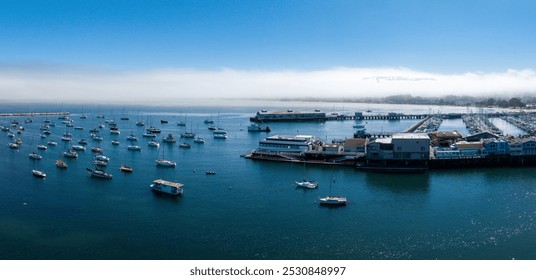 Monterey, California's marina is filled with sailboats and small vessels. Waterfront buildings line the coast, with fog hovering over the horizon. - Powered by Shutterstock