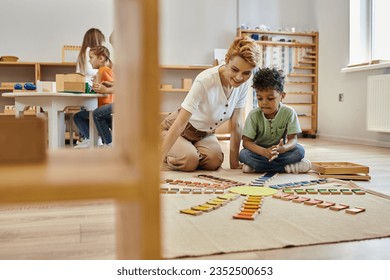 montessori material, african american boy playing educational color game near cheerful teacher, kids