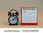 Monthly desk calendar for December 2024 year on wooden table with black alarm clock.