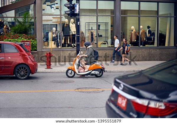 MONTREAL, CANADA - SEPTEMBER 6, 2018: Elderly\
woman on a moped on Montreal street, waiting for a red light in the\
of a stream of cars on High\
Street