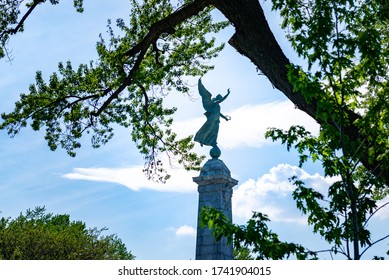 Montreal Quebec Canada May 26 2020: Monument To Sir George-Étienne Cartier In Mount Royal Park, Framed Though Tree Branches With Blue Sky And Clouds  