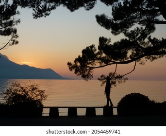 Montreux,Switzerland - October 23,2011 - Scenic Silhouette Sunset View Of Montruex On The Lake, Woman Spend Their Peaceful Solitude Time Walking Alone Along Lakeside Which Hugs The Bank Of Lake Geneva