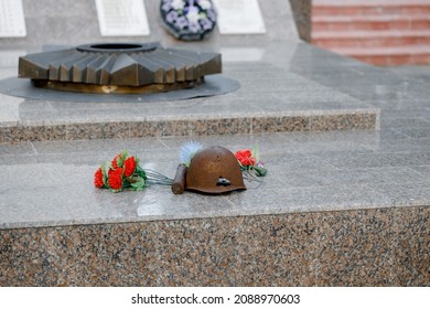 Monument of the Great Patriotic War. A helmet pierced by a bullet, a bullet and flowers lie on a granite slab near the eternal flame. 