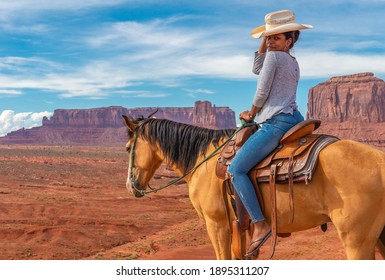 MONUMENT VALLEY NAVAJO TRIBAL PARK, USA - JULY 27, 2018: Young African american woman on horseback by John Ford viewpoint with view over West Mitten butte and Mitchell mesa.
