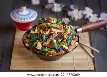 Moo shu pork. Homemade Chinese stir-fry dish made with marinated pork, cucumber, egg scramble, chopped scallions and black wood ear mushrooms served in in frying pan. Selective focus, horizontal.