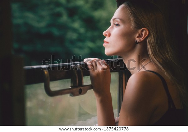 Mood atmospheric lifestyle portrait of young\
beautiful blonde hair girl looking out of window from riding train.\
Pretty teen enjoying beauty of nature from moving train car in\
summer. Travel concept.