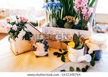 mood board spring table setting, wooden vase with blooming bulbous flowers in a wooden vase with the inscription Hello spring, on a wooden table, on which there is a figure of a blue bird and a wooden