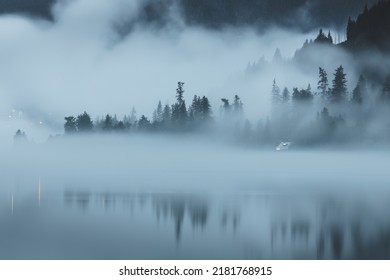 Moody, atmospheric evening fog over Kootenay Lake in Nelson, BC, Canada, with a remote, secluded cabin along the waterfront.