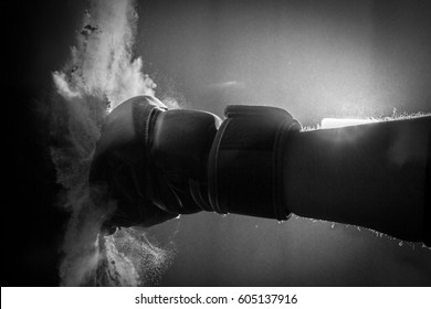 Moody Black & White Close Up Action Photo of a Boxing Glove Hitting a Punching Bag - with an Explosion of Dust on Contact in a Foggy, Shadowy Room